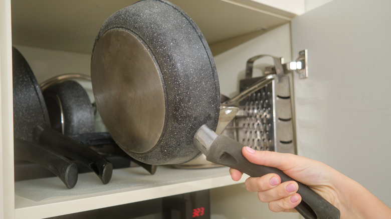 A hand putting a pan away into a cupboard