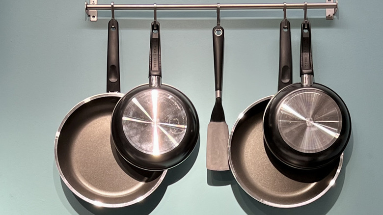 Frying pans hanging on wall along with a spatula