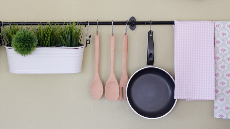 A hanging rack with towels, pan, plants and wooden utensils hanging on wall