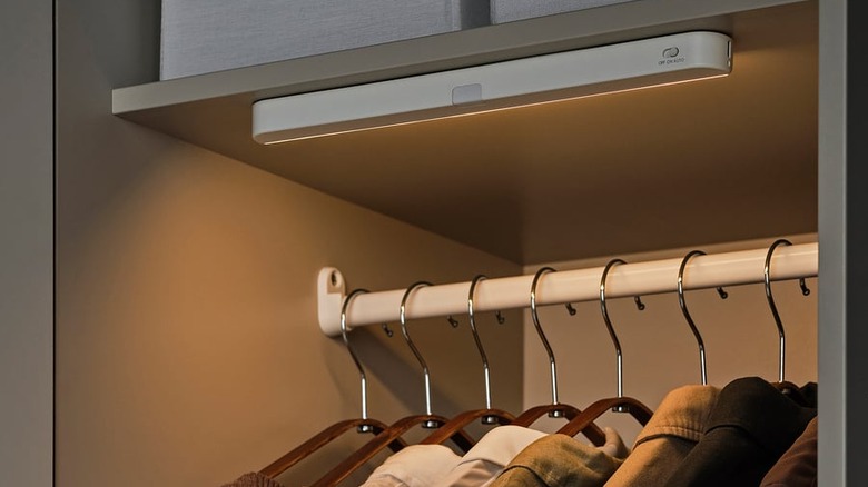 An IKEA K﻿ÖLVATTEN light strip mounted to the ceiling of a gray wardrobe with clothes hanging inside
