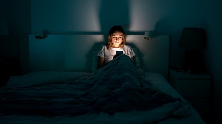 A person looks at their phone in a darkened room, with the only light coming from the phone