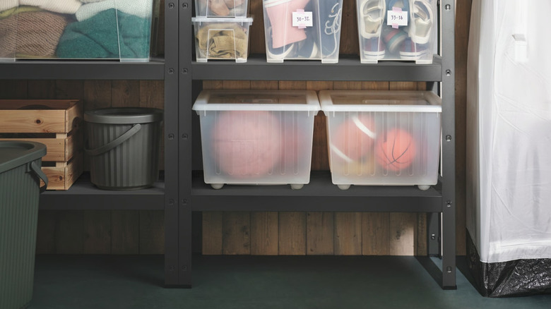Two IKEA VESSLA bins full of sports balls on a shelving unit in a garage..