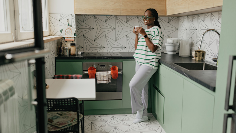 Woman standing in a small kitchen with light green cabinets