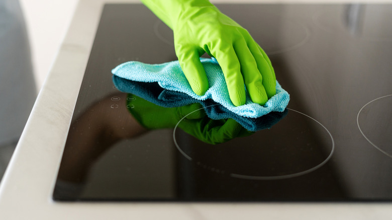 Gloved hand of person wiping a glass stove with a cleaning cloth