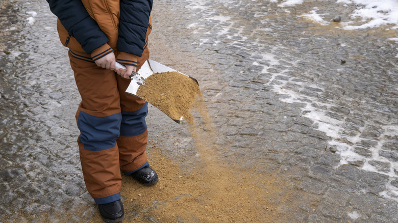 A person sprinkles sand on an icy sidewalk.