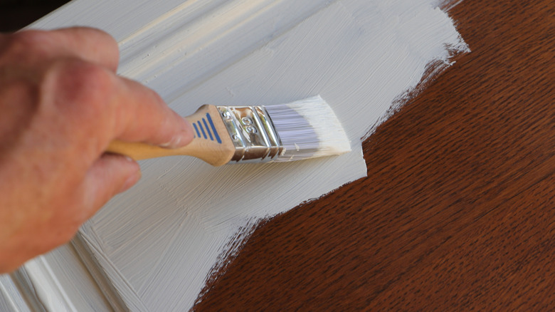 Someone painting a cabinet door with white paint and a paintbrush