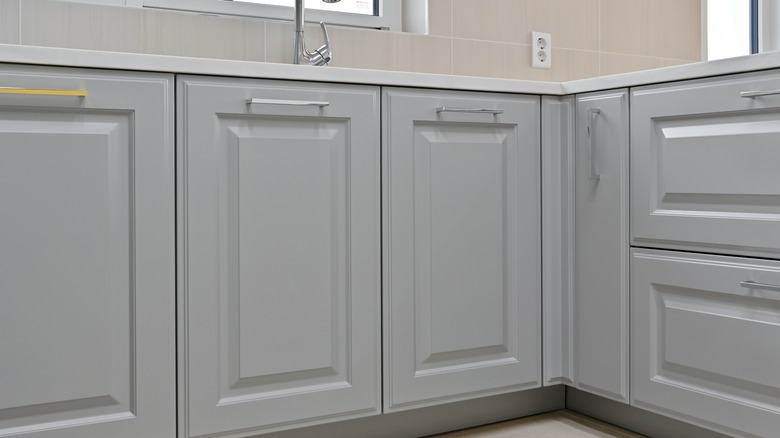 Light grey kitchen cabinets and drawers in a modern kitchen with beige tile walls