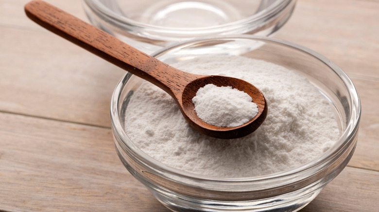 bowl of baking soda with wooden spoon sitting on a wooden table.