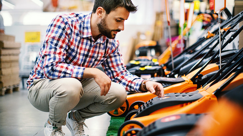 Man squatting while inspecting lawn mowers to buy