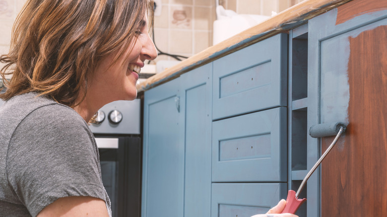 A person painting the kitchen cabinets blue