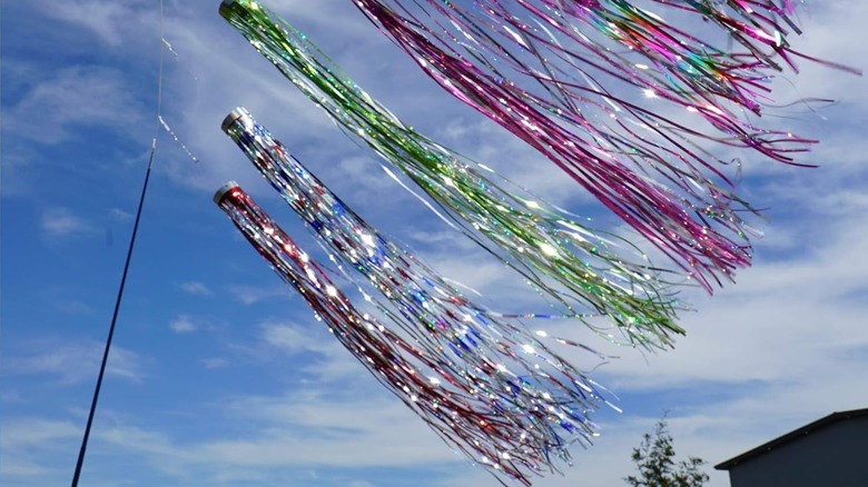 Windsocks made of holographic streamers hung from a pole in a backyard.
