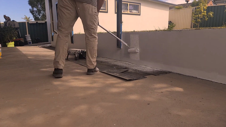 Person painting a concrete retaining wall with elastomeric paint with a hand roller