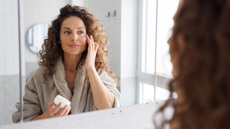 woman uses borderless mirror to apply lotion