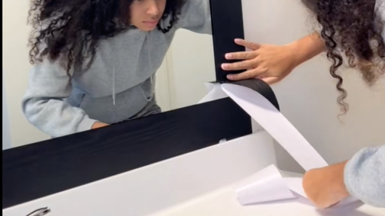 person applies wood grain tape to mirror to create a border