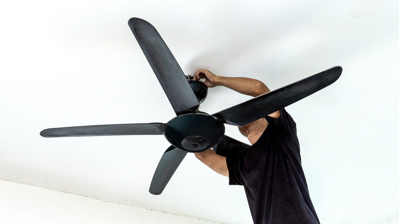 A man installs a ceiling fan in a white-walled home.