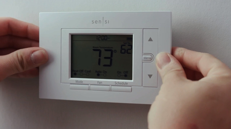 Two hands putting on the Sensi Smart Thermostat on a white wall