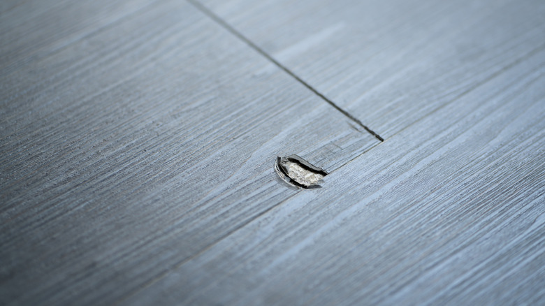 Broken vinyl flooring with a visible scratch.