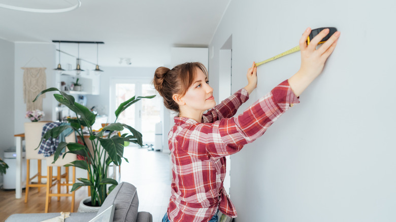 Woman measuring the wall before installing frame molding