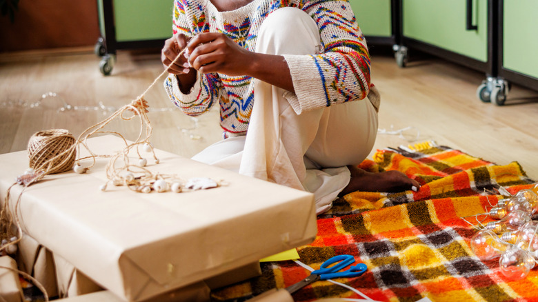Person wrapping gifts with brown paper and twine, while sitting on a blanket on the floor