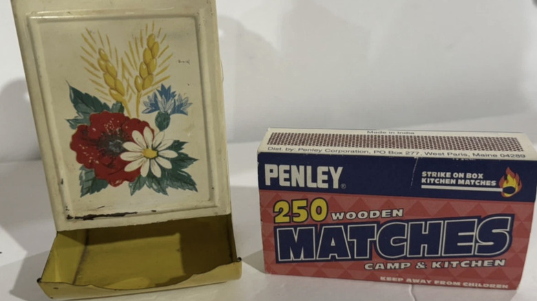 A vintage yellow matchbox holder with a floral design next to a box of large matches.