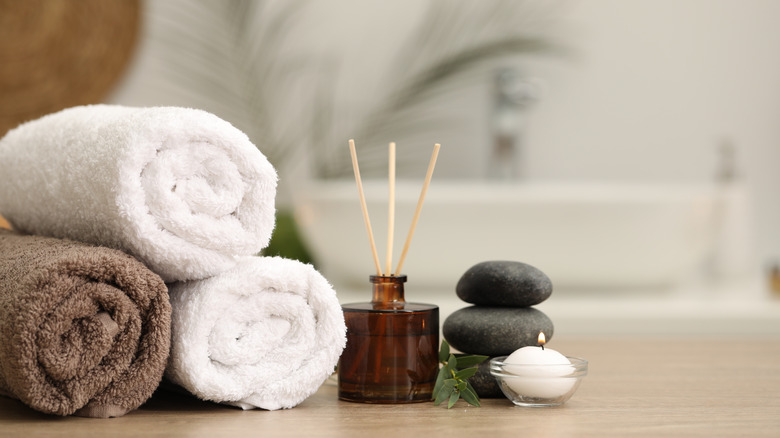 Bathroom towels rolled up on the counter next to a reed diffuser and some stacked stones