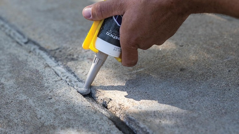 A person uses a tube of concrete caulk to fill a crack in a driveway.