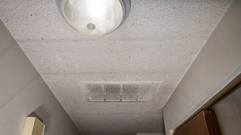 White popcorn ceiling with dirty air vent and ceiling light with glass globe.