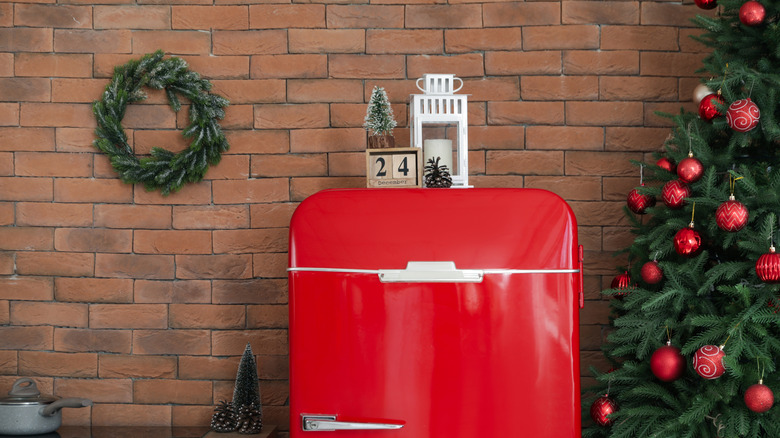 A red fridge surrounded by a Christmas tree and festive decor