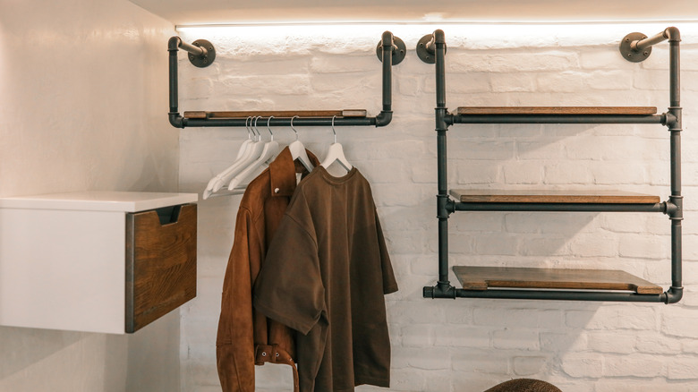 Shelves and clothes hanging rod made from metal pipes attached to a painted brick wall.