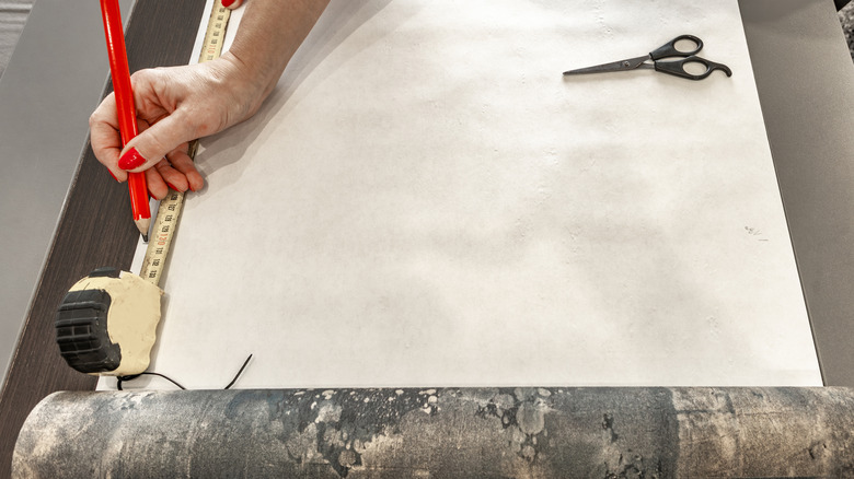A woman measures peel-and-stick wallpaper to cut