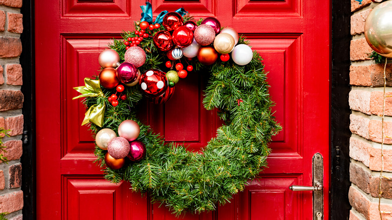 A wreath decorated with glass ball ornaments hangs on a door.