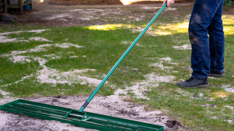 A man raking over a patch of soil that he's added sand to for topdressing.