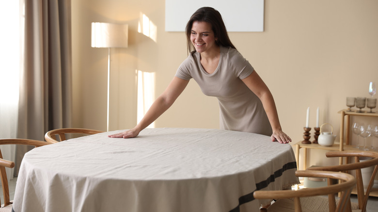 A woman smooths a tablecloth on a dining table