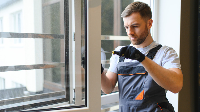 A man using a screwdriver to repair a window