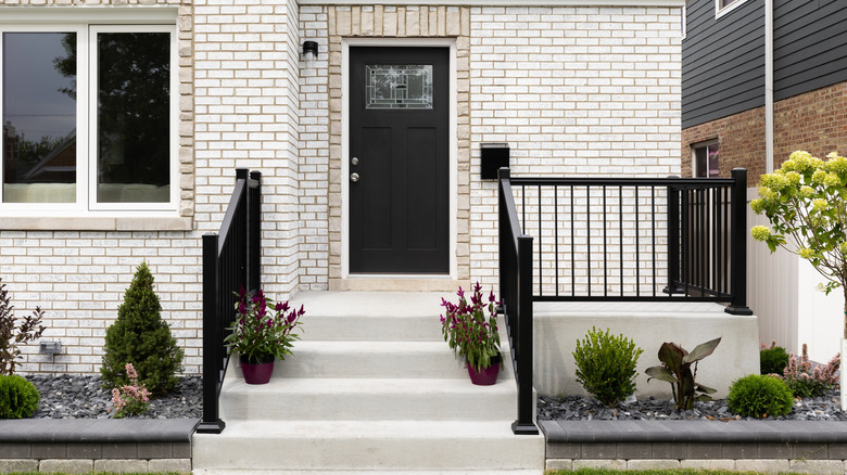 A front door detail on a white brick home with concrete steps and black railing leading to a black front door with a mosaic window.