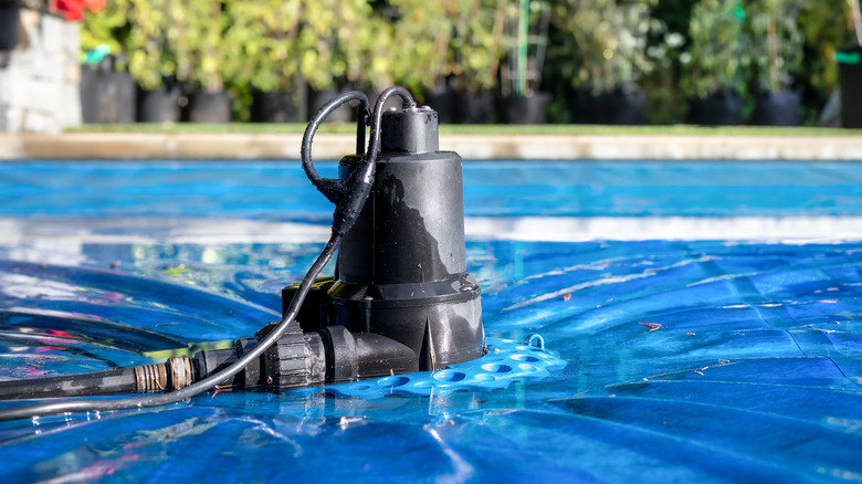 A pool cover pump on top of a blue inground pool.