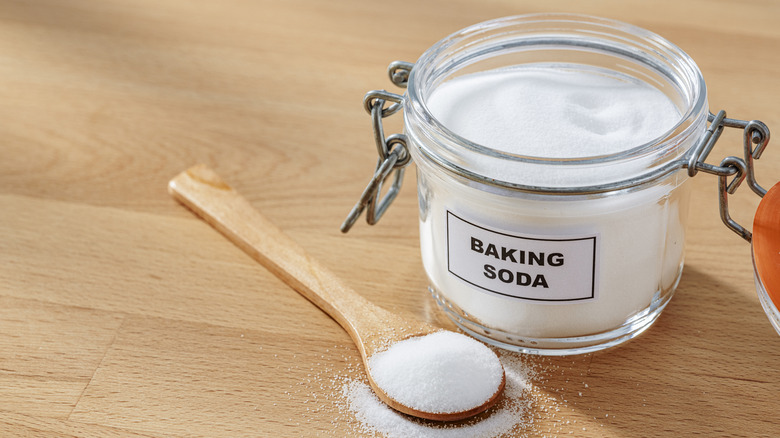 A jar of baking soda on a table alongside a wooden spoon