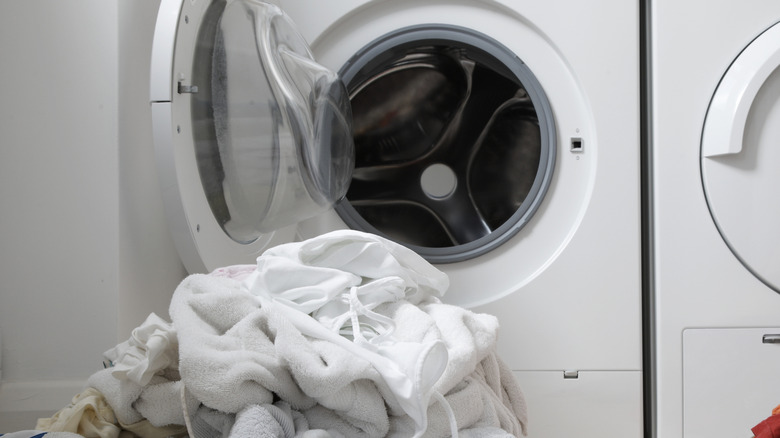 A pile of white clothes on a laundry room floor in front of a washing machine