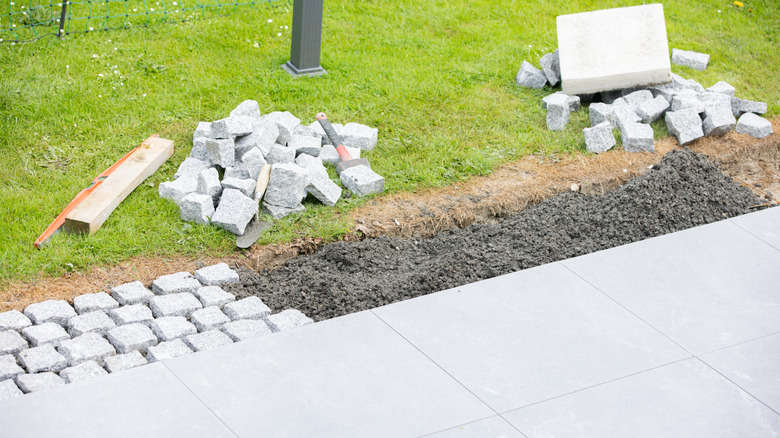 Putting down paving stones along the edge of a cement patio.