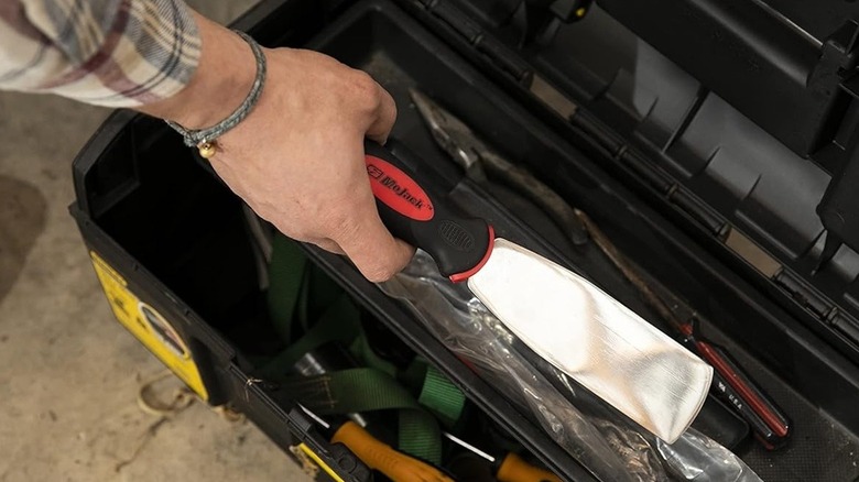 Person holding the MoJack scraper tool near a toolbox