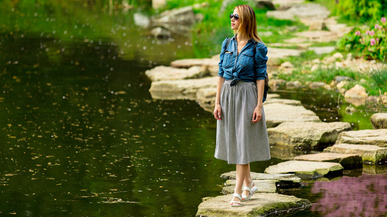A woman walking across stepping stones in a tranquil pond in a garden.