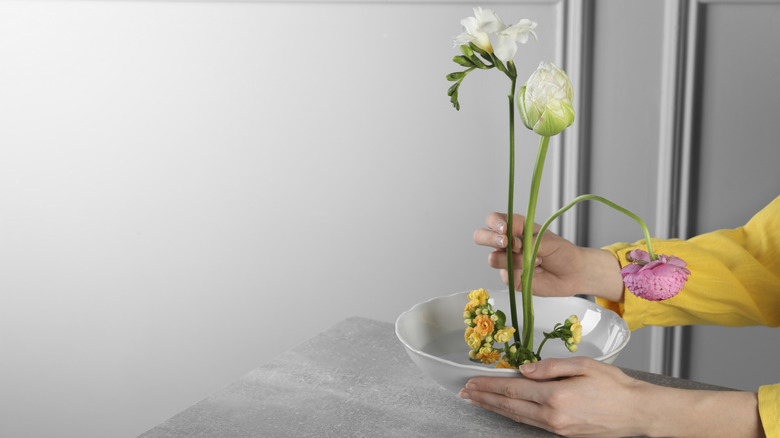 A person creating an ikebana style floral arrangement