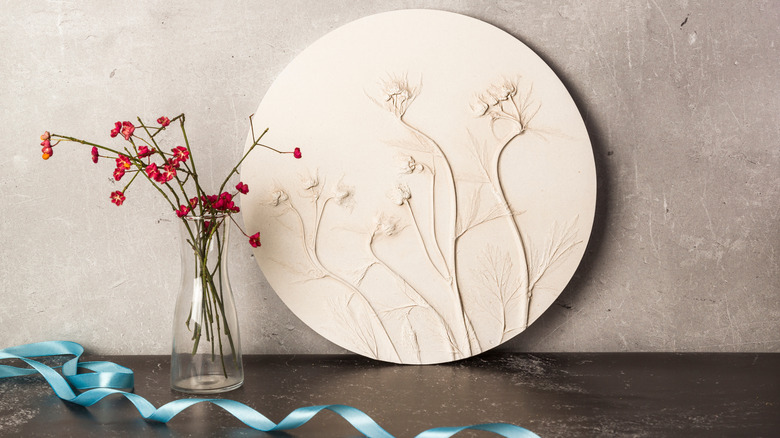 A bas relief of delicate flowers next to a vase of similar flowers.