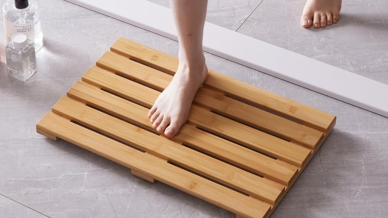 A foot steps onto a structured bamboo bath mat on a bathroom floor.
