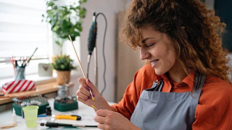 A woman holds a paintbrush as she works on a crafts project