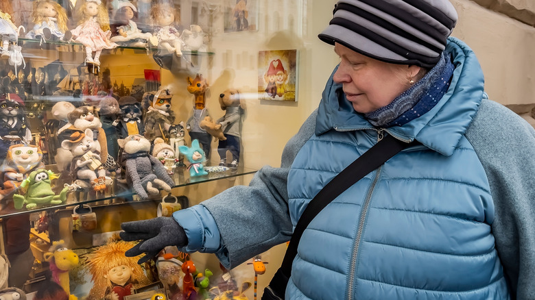 A woman in warm winter clothing points at some toys in the window of a thrift store.