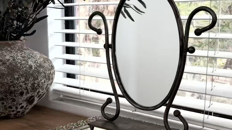 A thrifted cast iron mirror sitting on a credenza in front of a window with open shades.