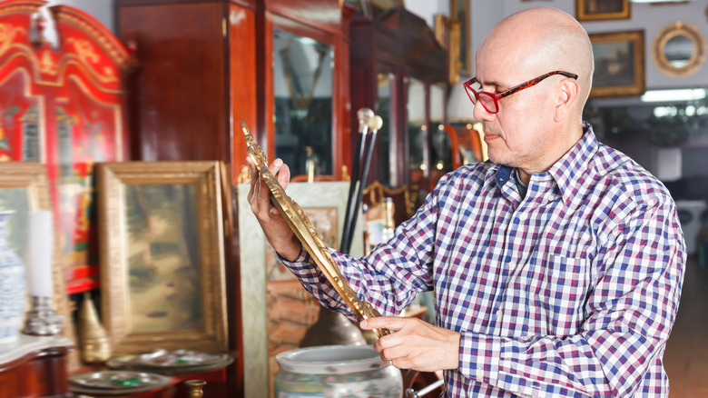 A man admires an ornate, gold-framed mirror in a thrift store.