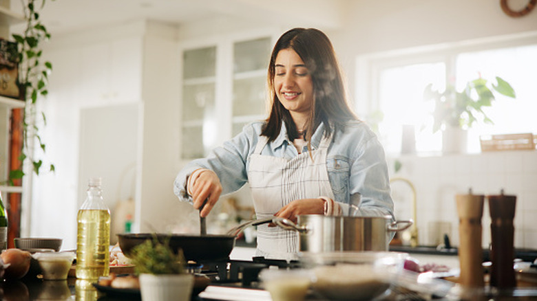 A young woman in an apron cooking at a stovetop in an airy, bright kitchen