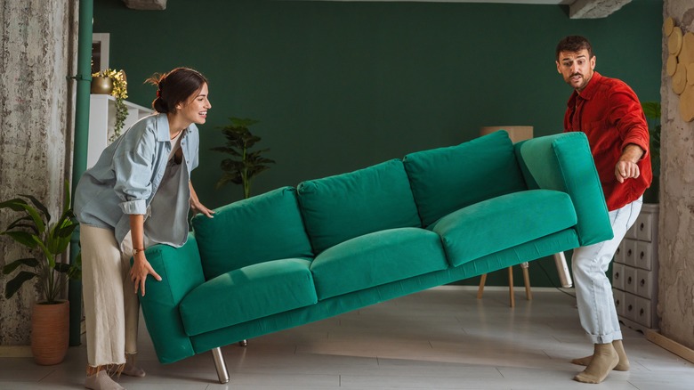 Couple lifting a green couch to rearrange the furniture setup